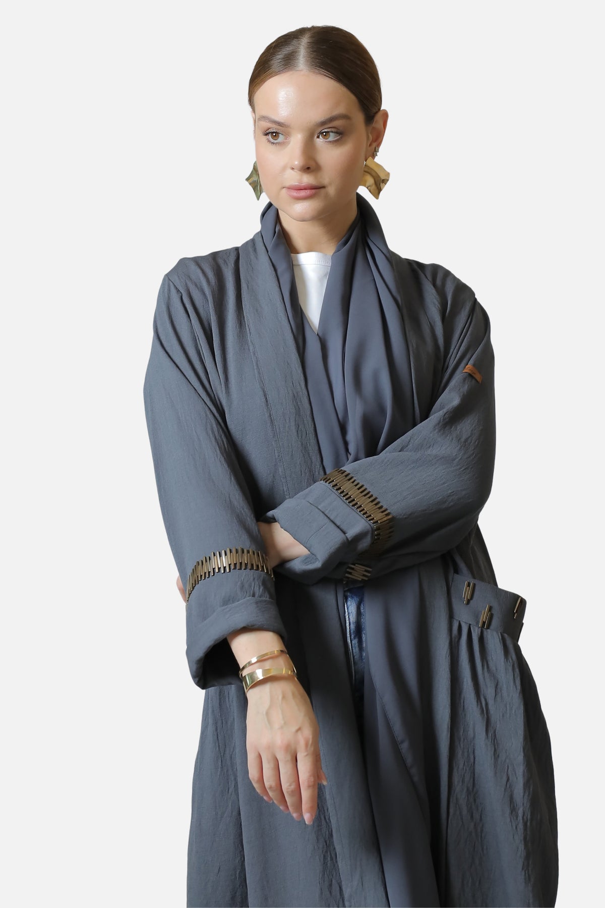 Gray linen abaya with gold-tone sleeve accents, shown with crossed arms.