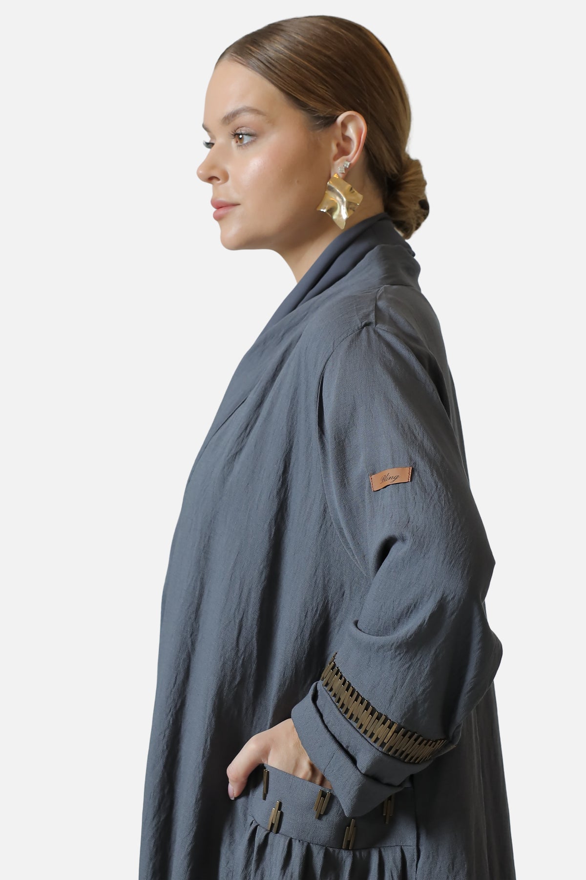 Side view of the gray abaya showing the sleeve trim, Bling label and decorated pocket.