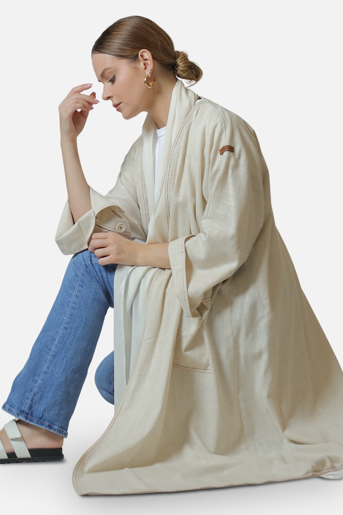 Ivory linen abaya with contrast stitch details — seated side view