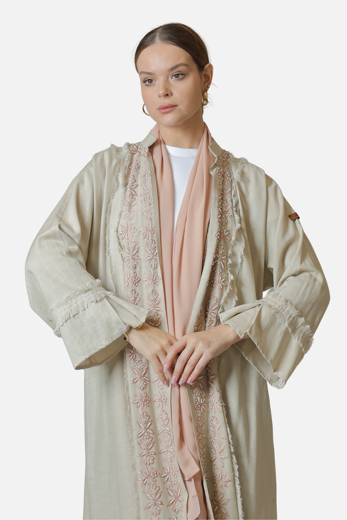 Front view of the beige linen abaya showing embroidered front edges, fringed cuffs and blush shaila.