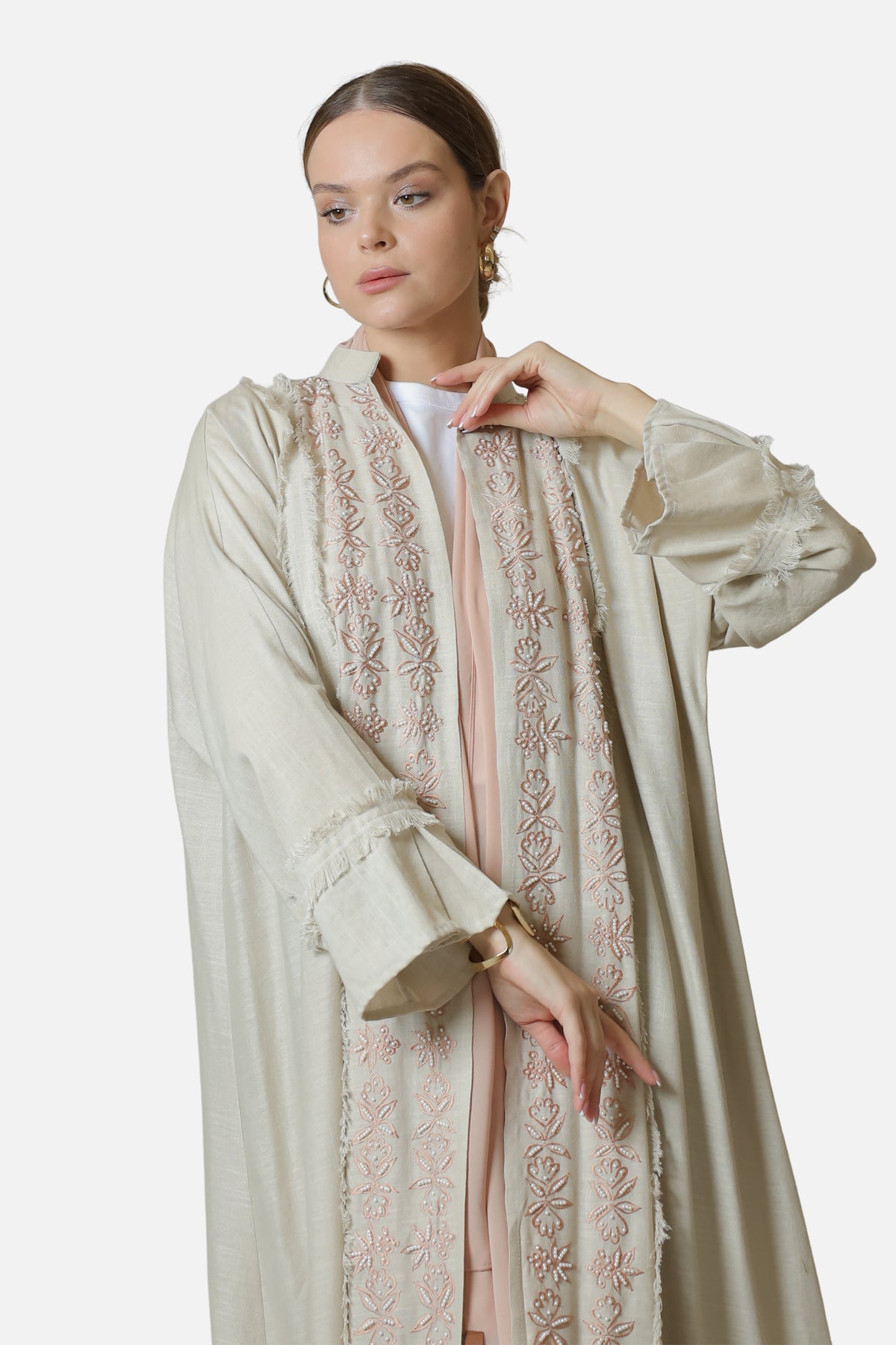 Model wearing the beige linen abaya open over a white top, showing the embroidered front panels.