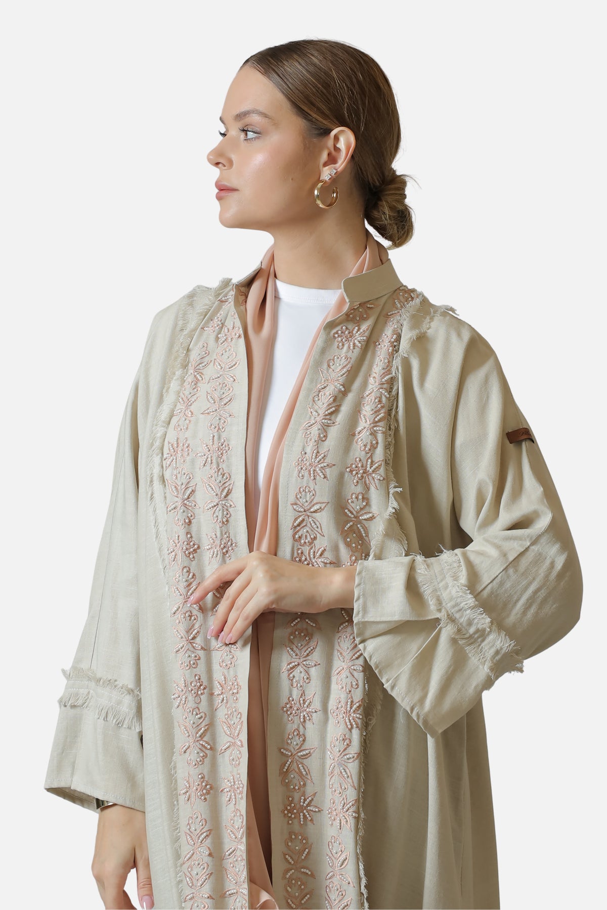 Side three-quarter view of the beige linen abaya showing the sleeve, fringed cuff and fabric drape.