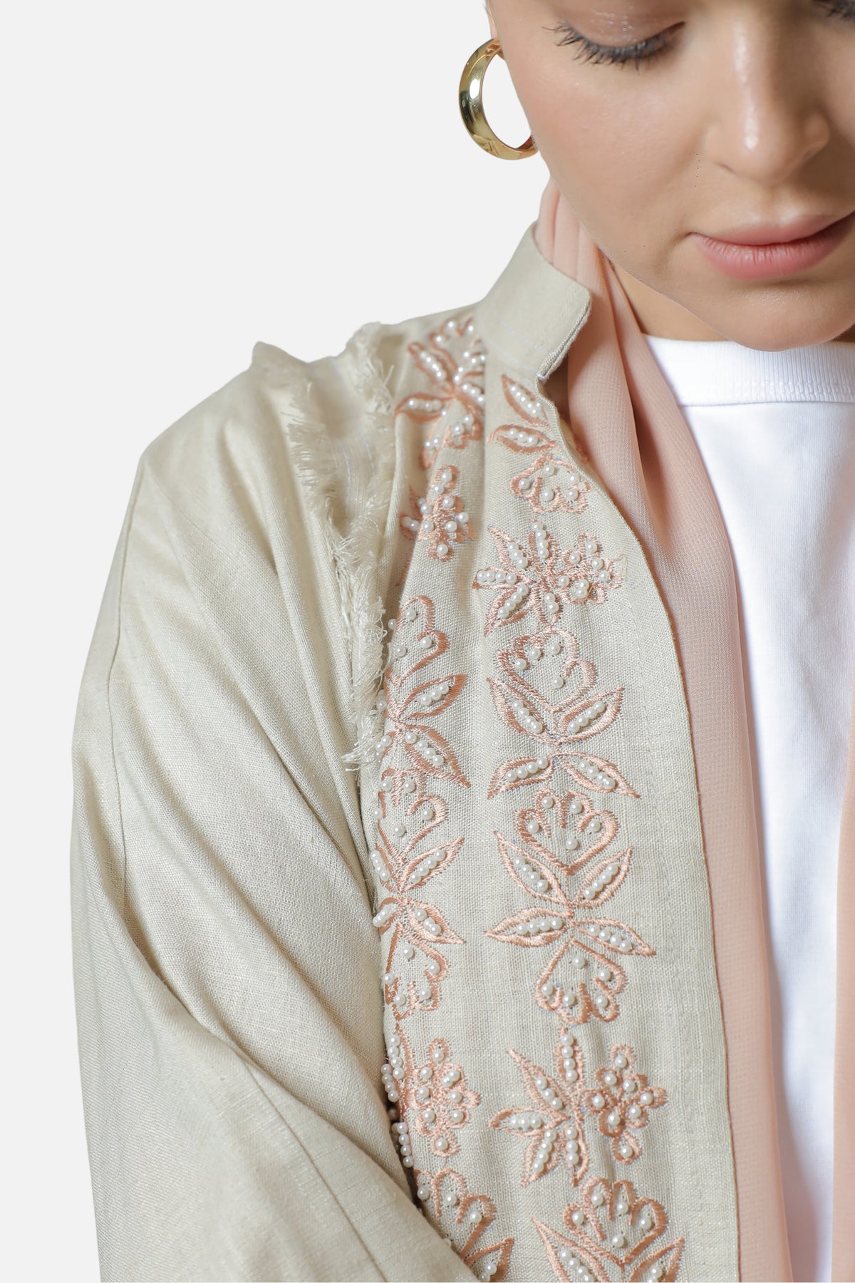 Close-up of the pearl-embellished floral embroidery along the front edge of the beige linen abaya.