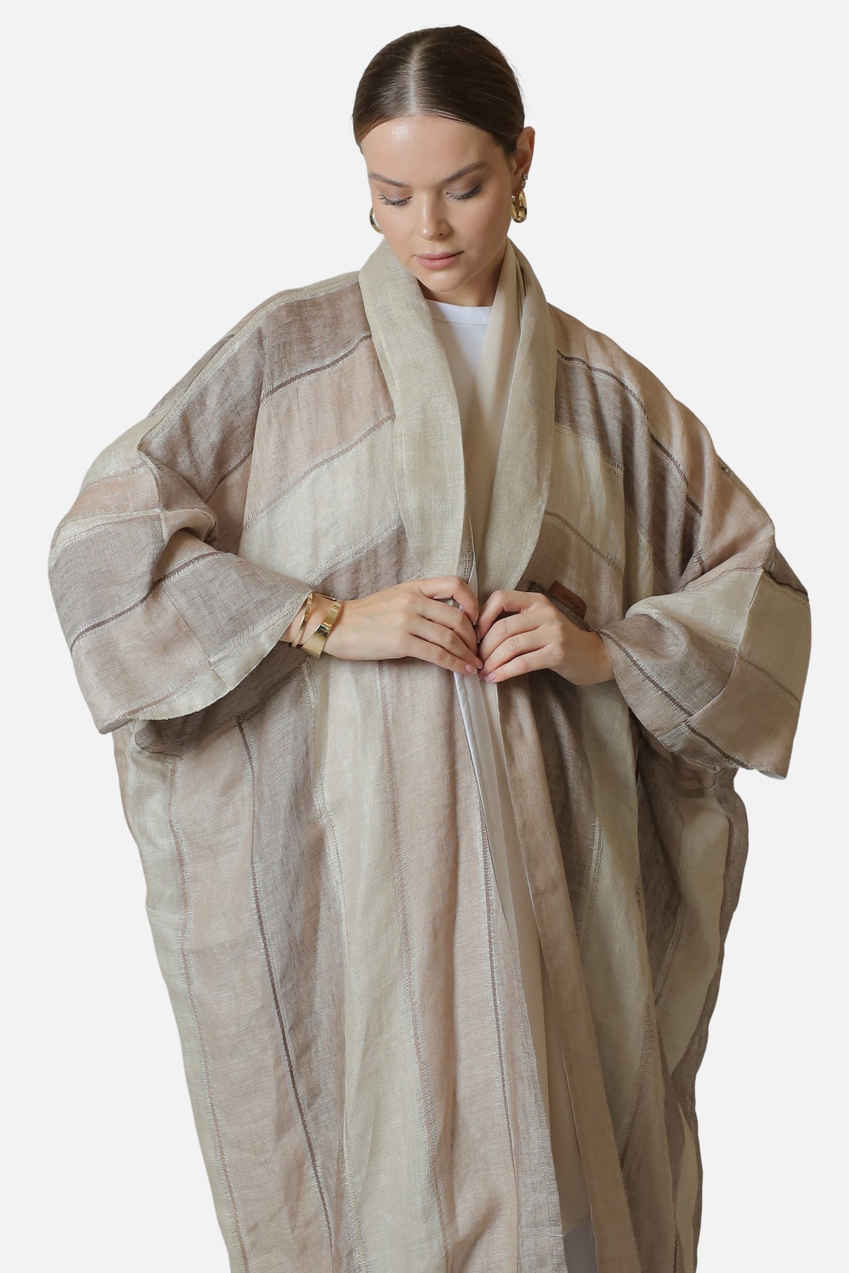 Neutral striped linen abaya shown from the front with hands together.