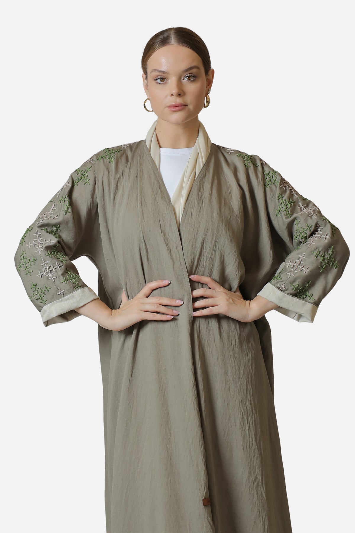 Beige linen abaya with light green sleeve embroidery, worn open over a white top.