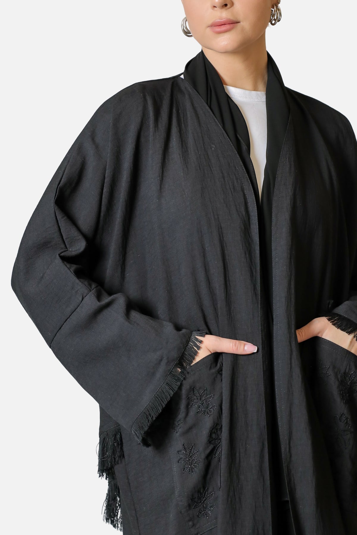 Patch pocket, tonal embroidery and fringed edge on the black linen abaya, close-up
