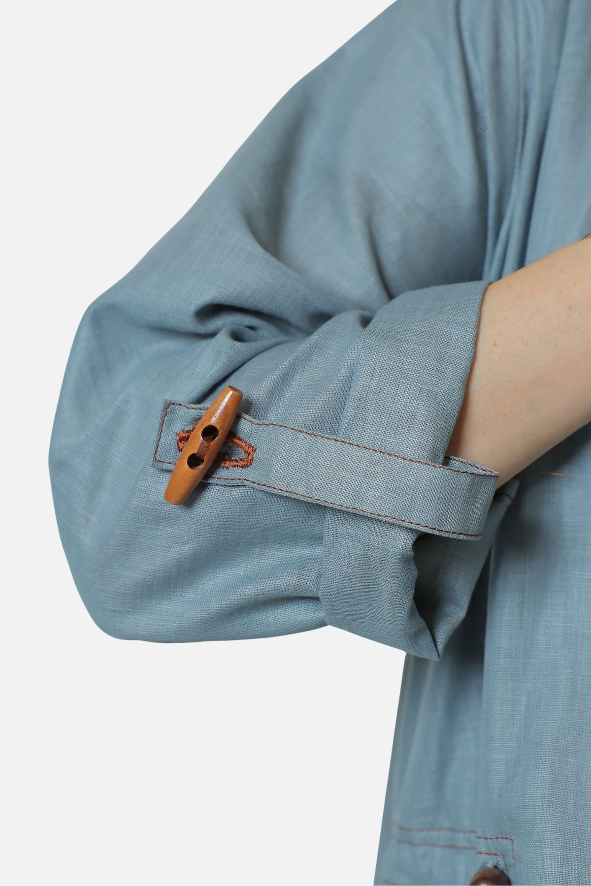 Close view of the wooden toggle and contrasting stitching on the blue-gray abaya sleeve.