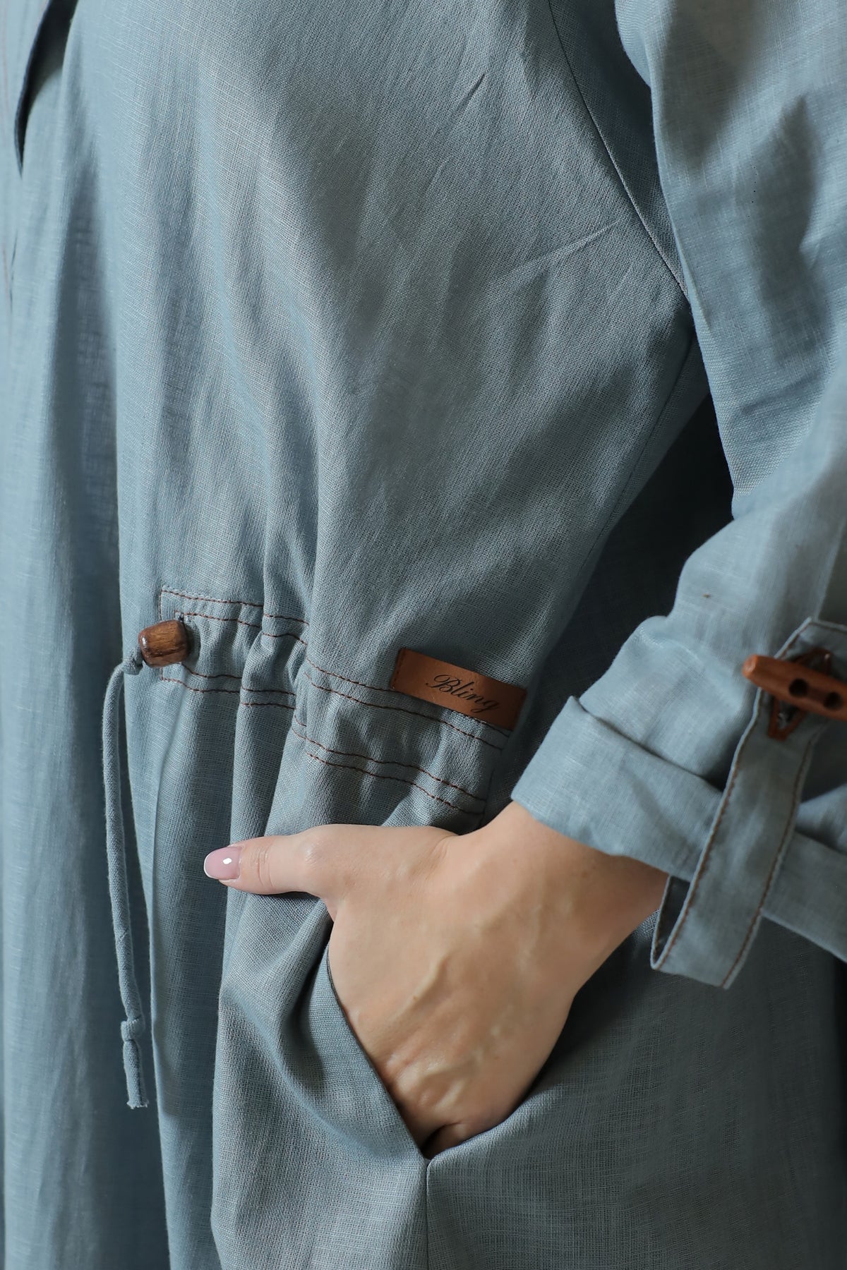 Detail of the blue-gray abaya pocket with wooden trim, contrasting stitching and Bling label.