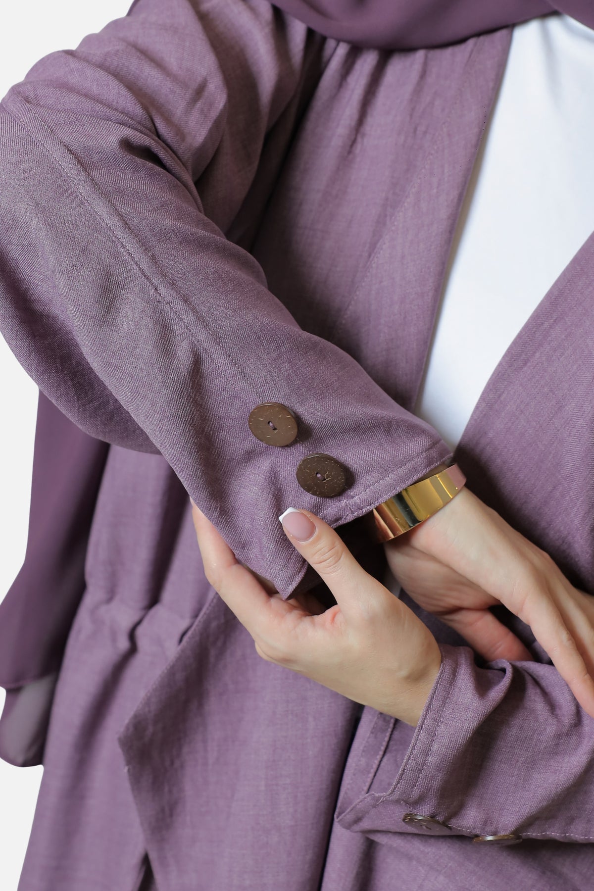 Close-up of two brown buttons on the purple abaya cuff, showing the stitching and fabric texture.