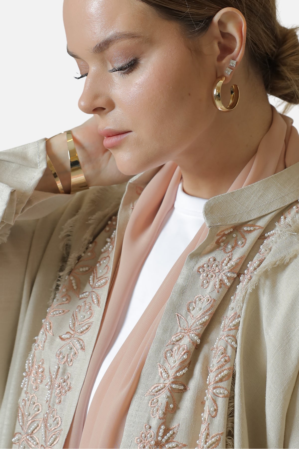 Detail of the beige linen abaya's embroidery and blush shaila at the shoulder.