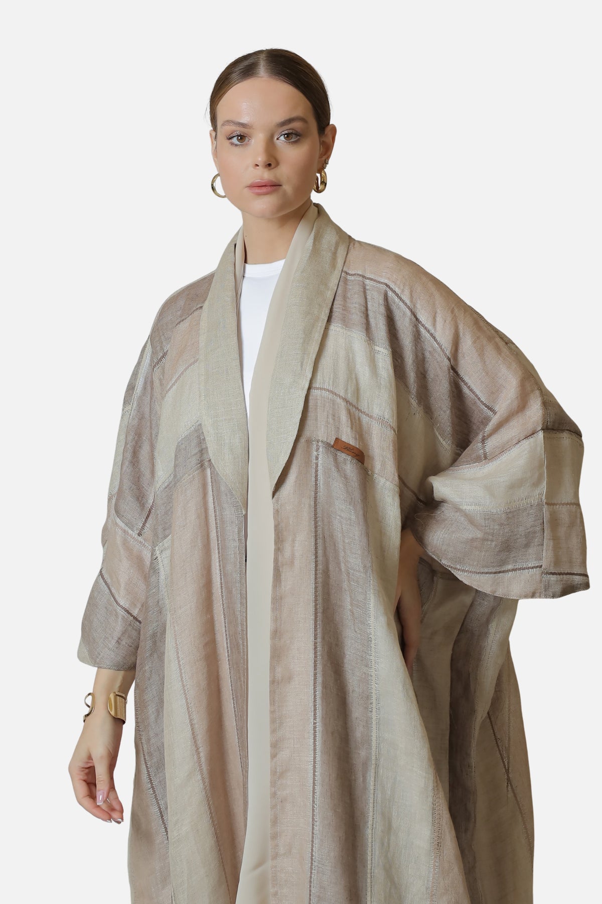 Front view of the neutral striped linen abaya showing its broad sleeves and Bling label.